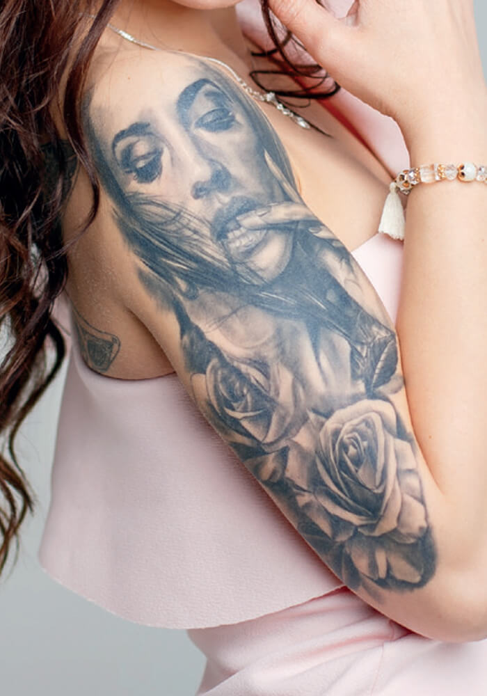 Frau mit pinkem Top zeigt Tattoobeispiel auf Arm