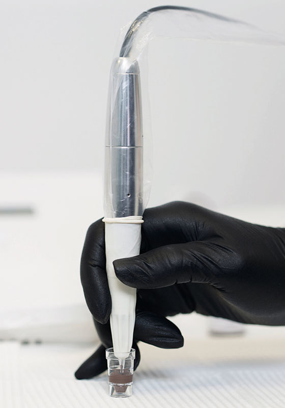 amiea Academy - Cartridge Detailaufanhme einer Hand mit schwarzem Latzexhandschu mit amiea-Handstueck und Farbe