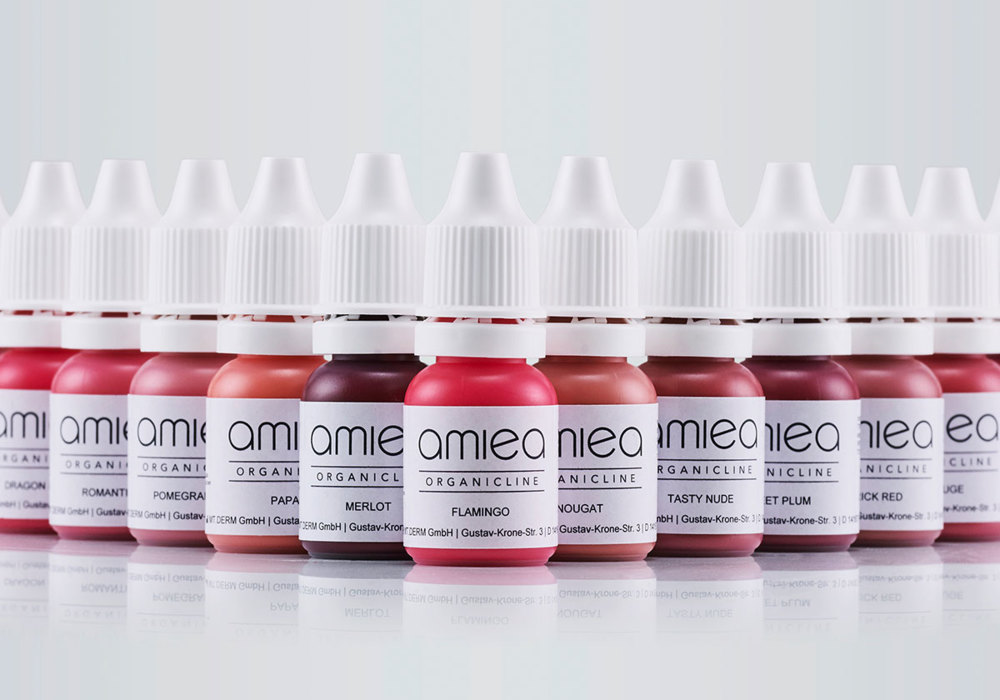 viele verschiedene amiea Organicline PMU Lippenfarbe-Flaschen auf grauem Boden mit grauem Hintergrund 
